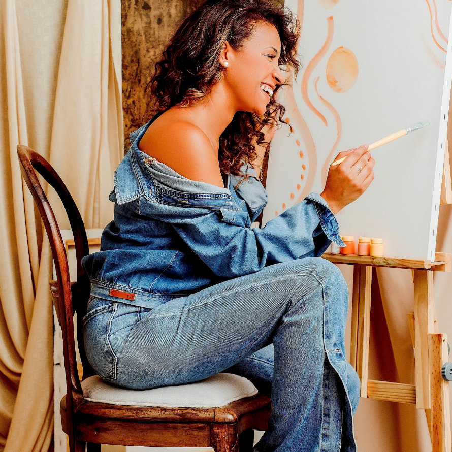 Künstlerin malt vor einer Staffelei sitzend.