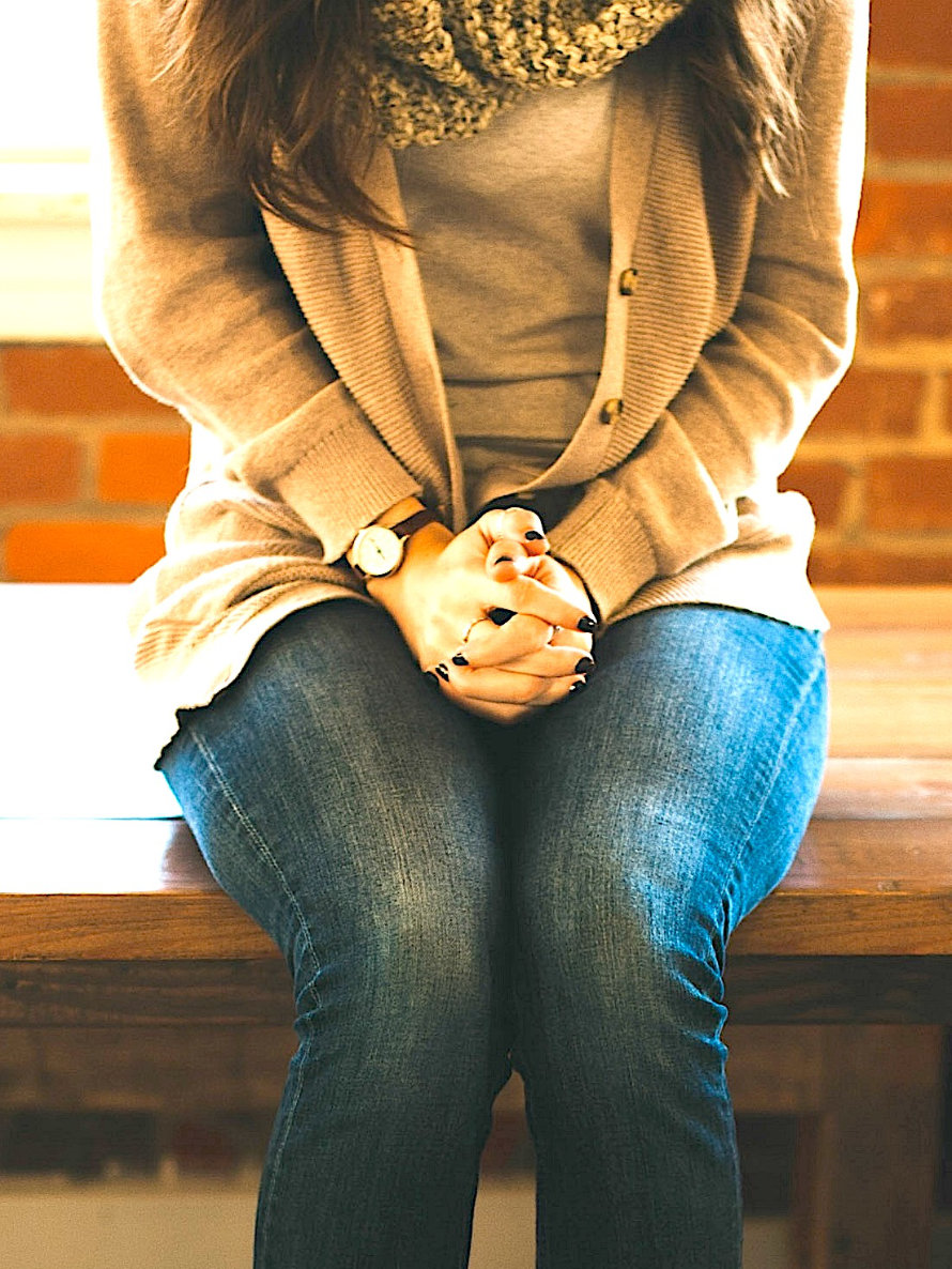 Frau in Jeans sitzt dringend pinkeln müssend auf einer Holzbank