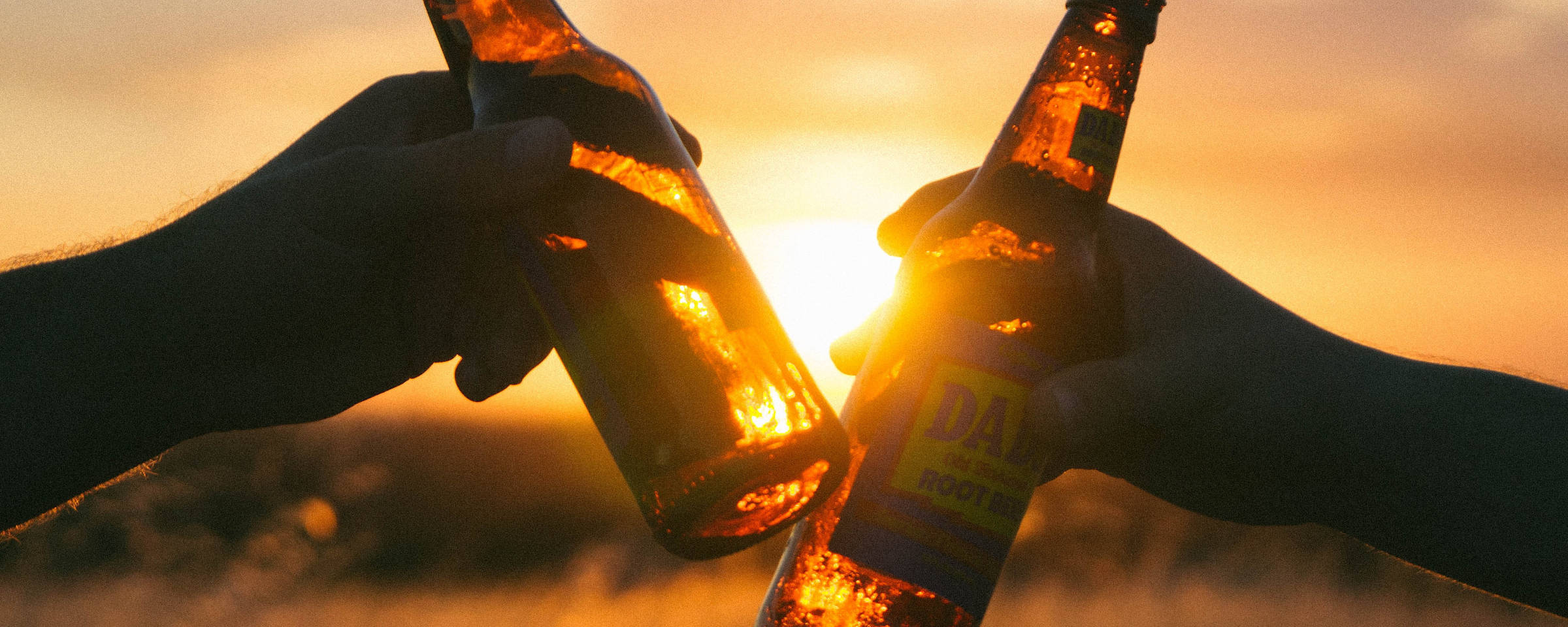 Anstoßen mit zwei Bierflaschen vor der untergehenden Sonne.