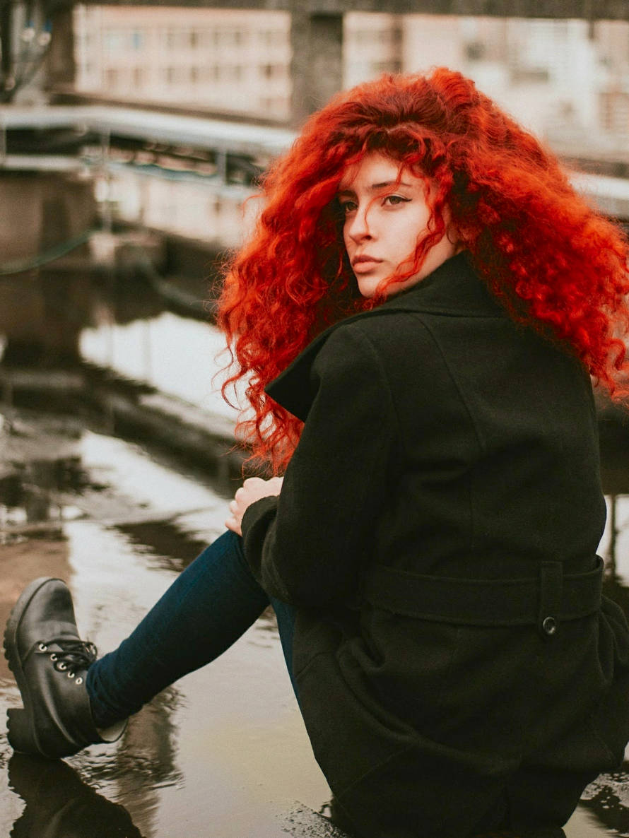 Symbolbild: Rothaariges Female-Model sitzt auf einem Hochhausdach in einer Regenpfütze.