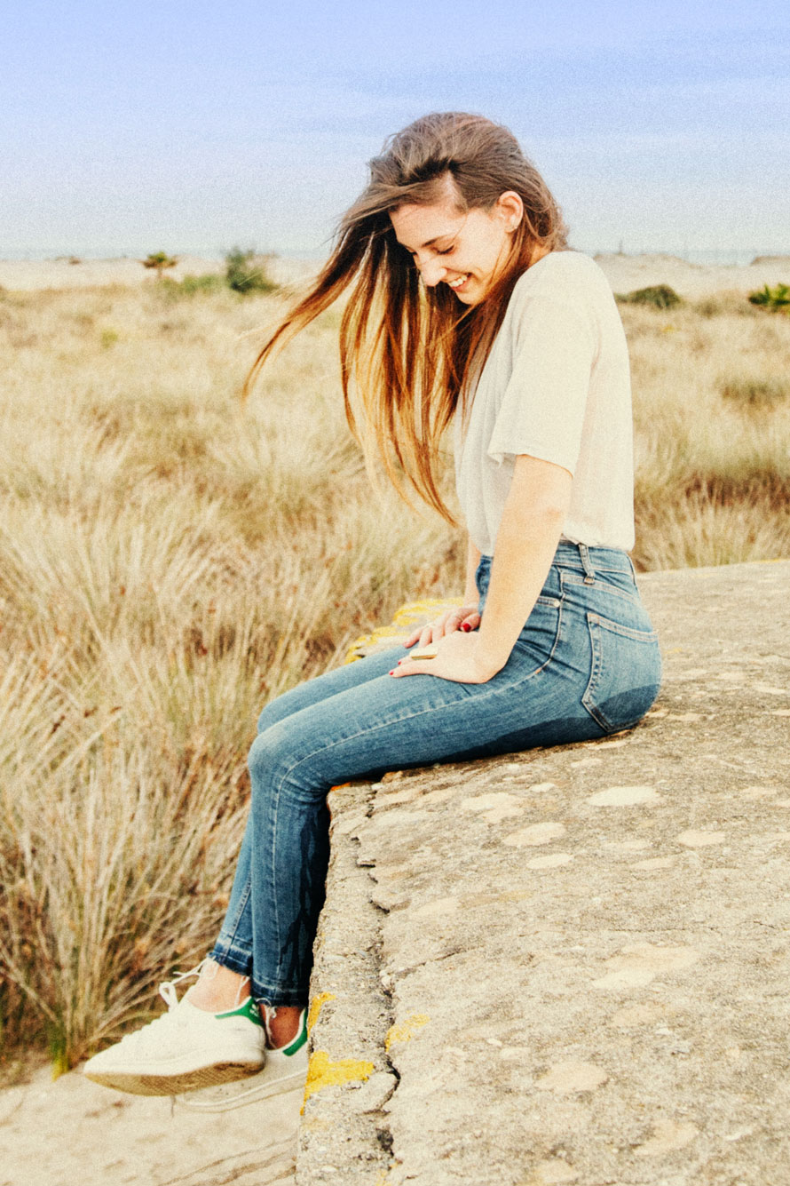 Junge Frau sitzt in der heißen Einöde mit nasser Jeans lachend auf einem großen Stein.