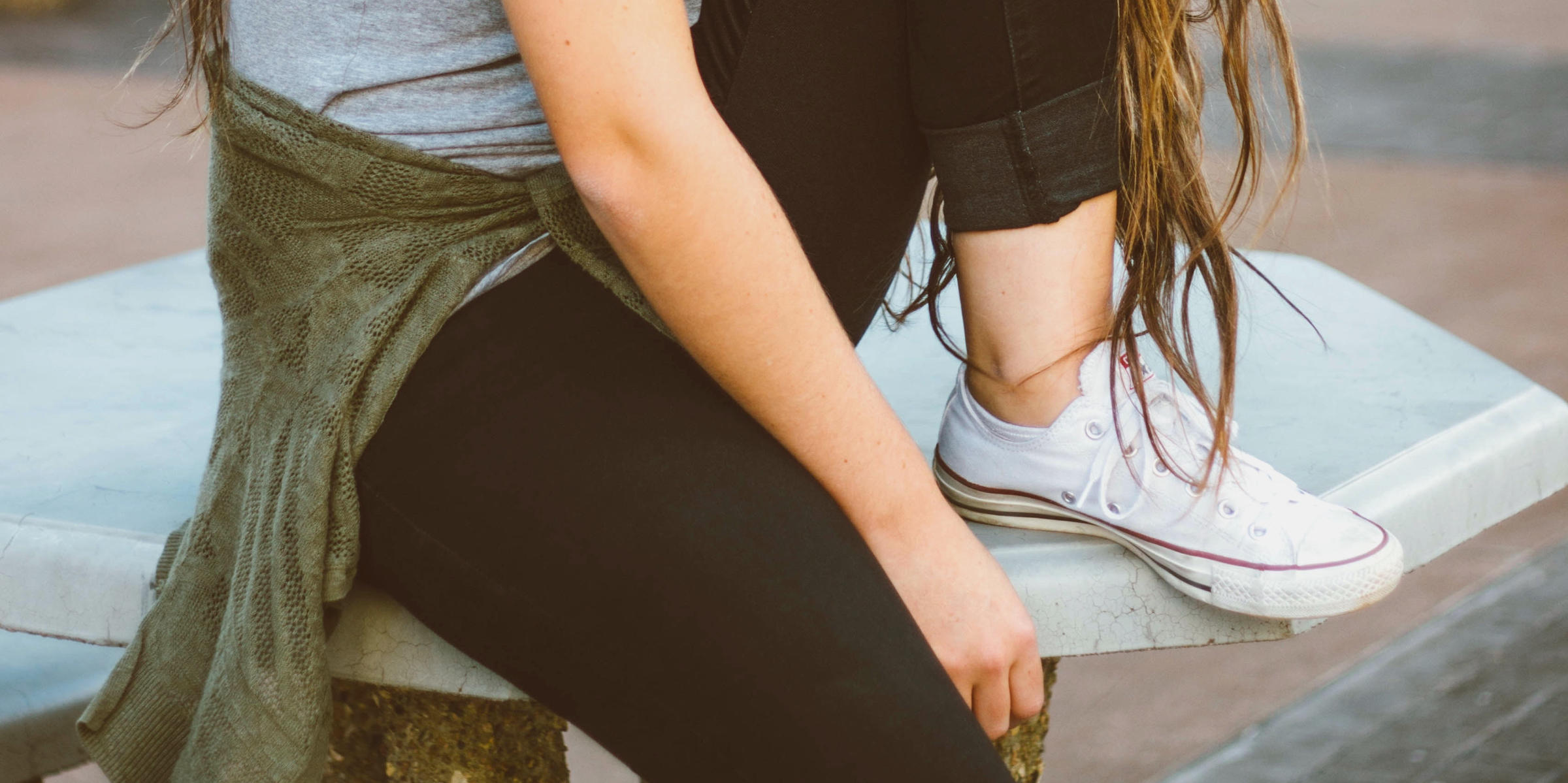 Junge Frau in schwarzer Jeans sitzt auf einem Allwettertisch und macht ihr großes Geschäft in die Hose.