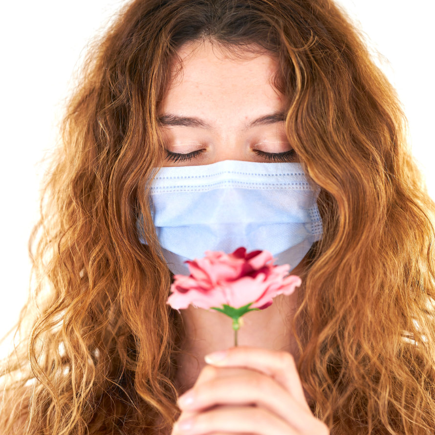 Junge Frau mit Mundschutz hält eine Blume in der Hand.