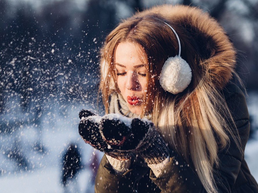 Junge Frau pustet vergnügt Schnee von ihren Handschuhen