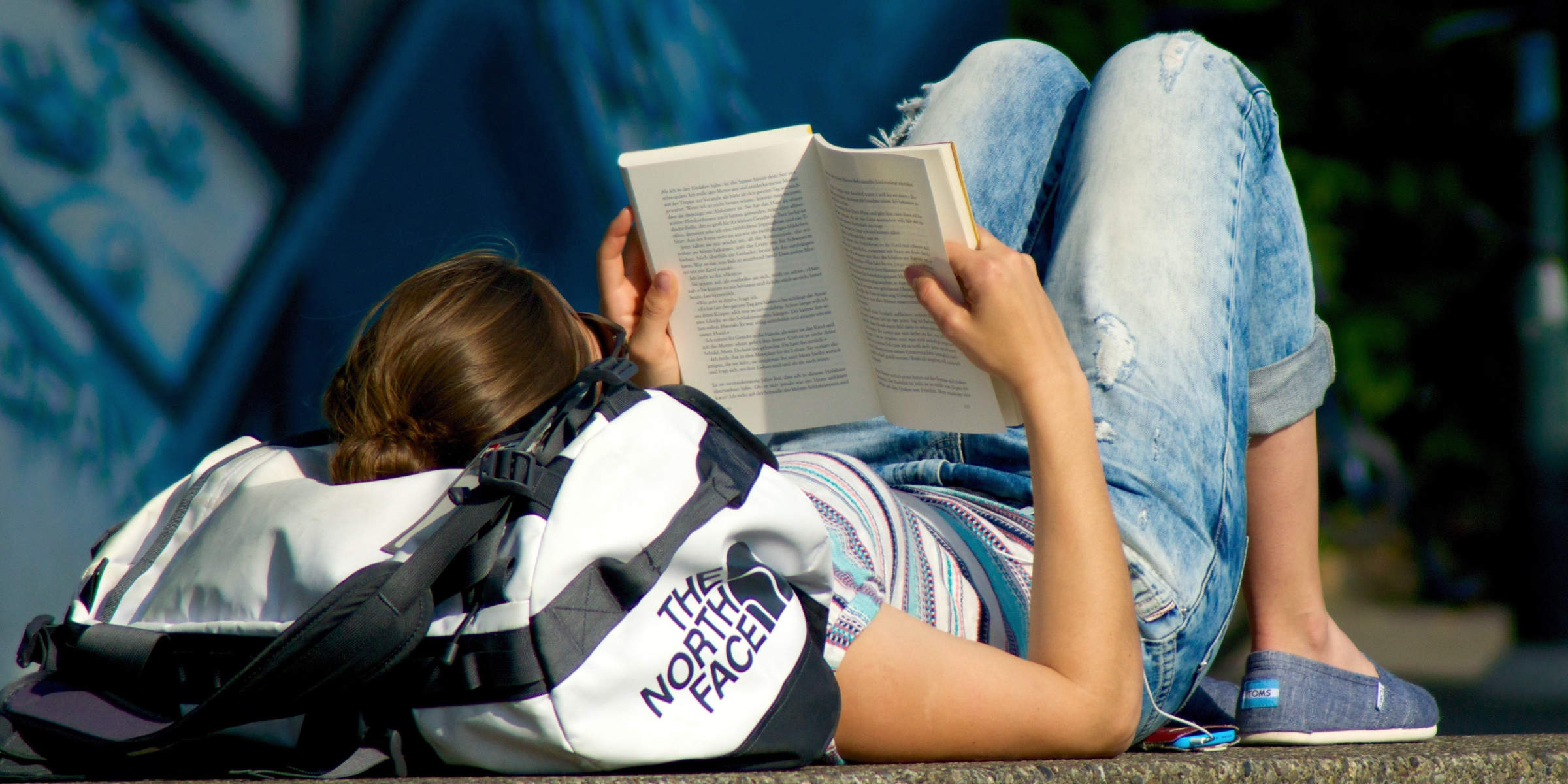 Junge Frau mit Windel unter der Jeans liegt in der Sonne und liest ein Buch.